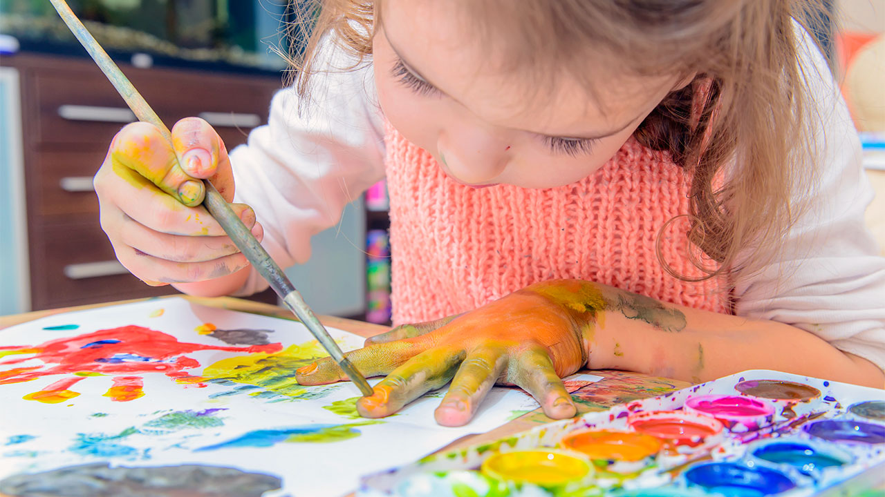  A preschool girl is painting her hand with yellow paint as part of a creative activity.